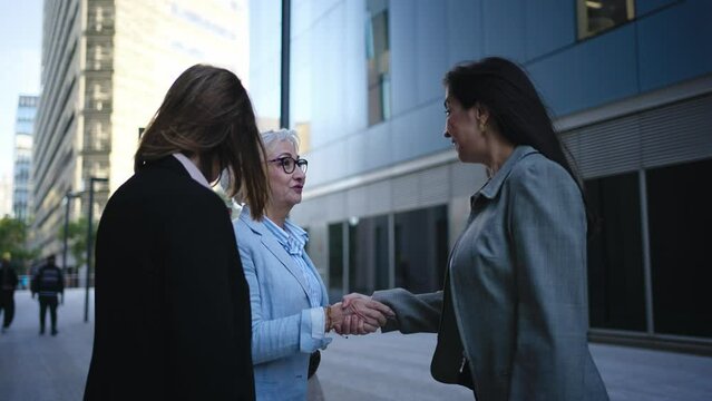 Group of mature business women close a deal by shaking hands outside corporate office. Three professional formal female talking confidently outdoors. Feminine empowered meeting lawyers 