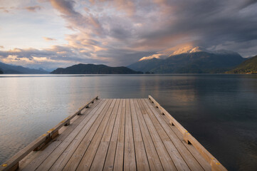 Wooden boat dock leading out to a lake with calm waters with a sunset sky. Harrison Lake, east of...