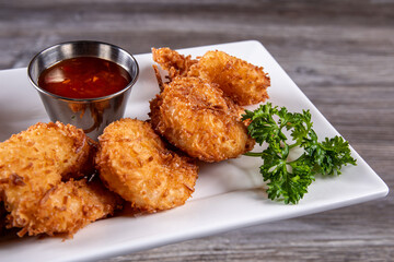 Close up of a plate of deep fried coconut shrimp with a red dipping sauce