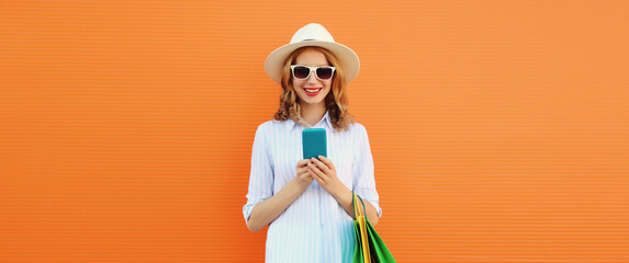 Beautiful happy young woman with phone with shopping bag in summer straw hat on orange background