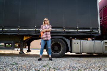 Confident young woman truck driver standing proudly with her arms crossed in front of the truck and...