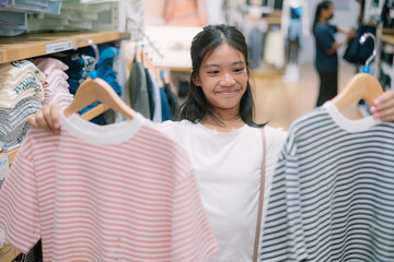 A young girl is holding up two shirts in a store