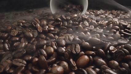 Close up of seed of roasted blending coffee falling from white cup with smoke come from bean. Macro...