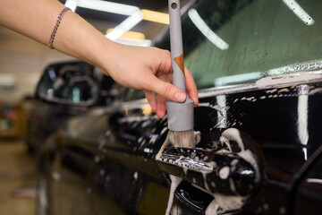 A person is cleaning a car windshield with a brush and water