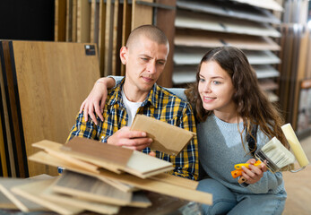 Modern family couple standing together with sample of laminated flooring in building store