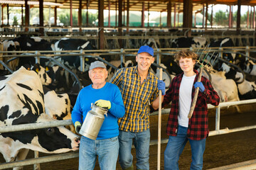 Successful elderly dairy farm owner with son and teen grandson posing together while working in...