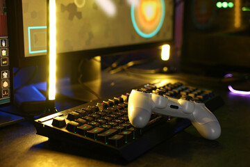 Playing video games. Computer keyboard and wireless controller on table indoors