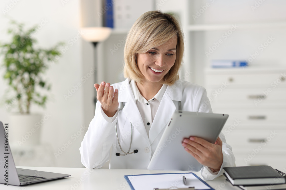 Wall mural Smiling doctor with tablet having online consultation at table in office