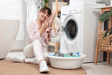 Happy young housewife with laundry near washing machine at home