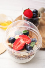 Tasty granola with berries, yogurt and almond flakes in plastic cup on white table, closeup