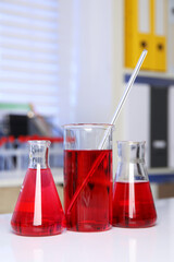 Laboratory analysis. Different glassware with red liquid on white table indoors