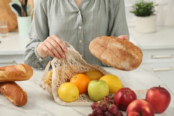 Woman with string bag of fresh fruits and bread at light marble table, closeup