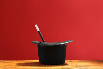 Magician's hat and wand on wooden table against red background