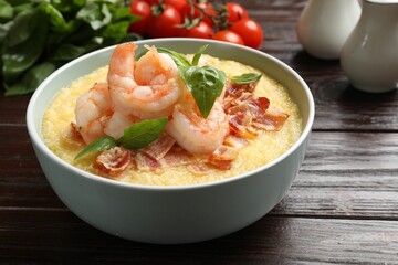 Fresh tasty shrimps, bacon, grits and basil in bowl on wooden table, closeup