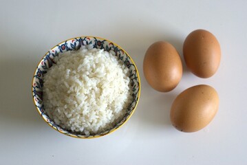A bowl of cooked rice and raw eggs on the table, cooking ingredient