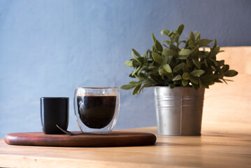 Hot black coffee cup on Wood office desk plant pot decor table blue background. Cup of Black Tea...