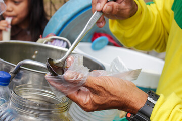 a man in a yellow shirt is pouring coconut milk and brown sugar into a plastic containing ice and...