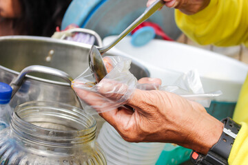 a man in a yellow shirt is pouring coconut milk and brown sugar into a plastic containing ice and grass jelly. grass jelly ice is the choice because it tastes sweet and cool in the summer.