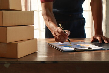 Middle aged Asian man, the owner of a small business, happily works on her laptop at home. She's managing orders and packaging products for delivery, showcasing success in e-commerce.