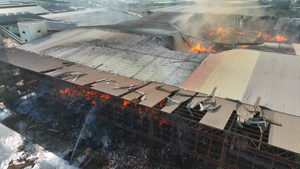 From above, witness a fierce conflagration ravaging an industrial structure. Flames dance amidst ruins, devouring all in their path. Smoke billows, obscuring the horizon in a haze of devastation.
