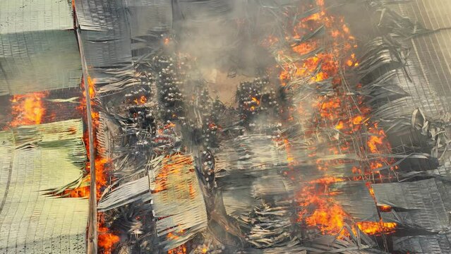 Aerial perspective unveils a harrowing scene, a raging inferno engulfs an industrial complex. Flames devour a collapsed roof, billowing thick smoke signals a dire catastrophe.
