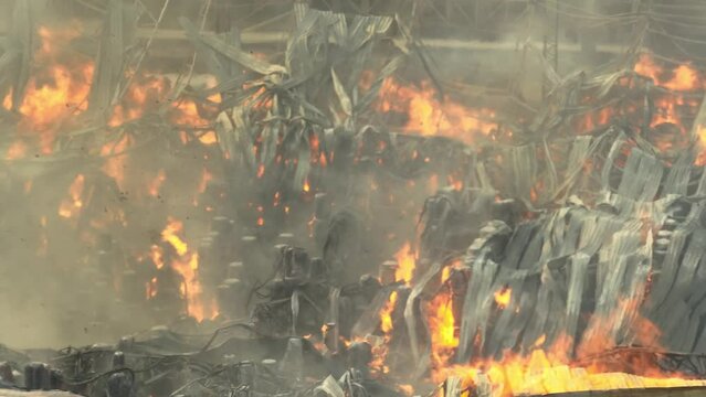 Intense flames devour the industrial site, metal structures twisted and collapsed in the inferno's grasp. Thick smoke shrouds the chaos, an ominous sight of destruction.
