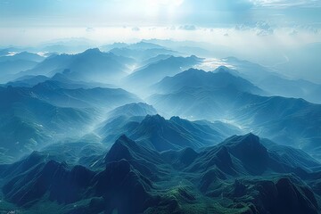 An aerial view of a mountain range. The mountains are covered in lush green forests, and the sky is a clear blue.