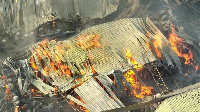 Aerial perspective captures an inferno ravaging an industrial complex, fierce flames devouring mangled metal and debris amidst billowing smoke, a scene of destructive chaos.
