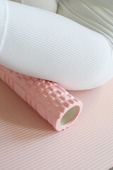 female legs in white leggings on pink massage roll and pink exercise mat, detail close up fitness photo
