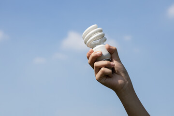 Recyclable electric waste held in hand up on sky background. Hand holding light bulb for recycle...