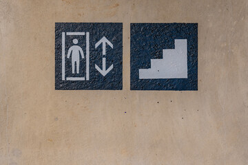 Close-up photo of a painted elevator and stairs sign on a concrete wall within a parking garage, car park.