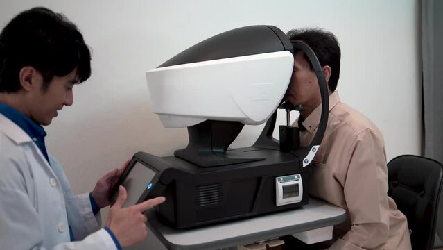 Male optometrist or optometry specialist checks the vision of a senior man using examination equipment within the optometry clinic.