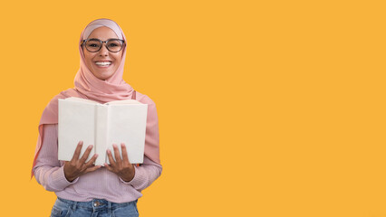 Reading hobby. Learning wisdom. Smart happy smiling woman in headscarf glasses with open book isolated on orange empty space background.