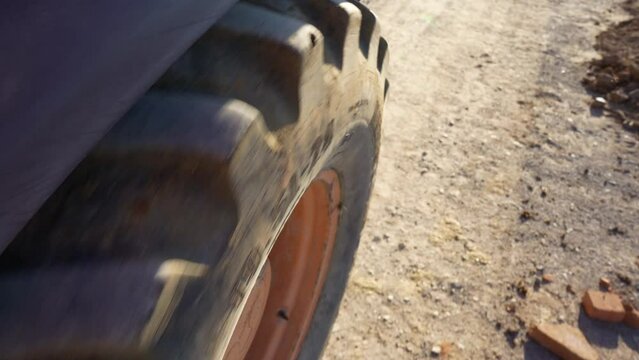 close up on a big wheel spinning, side view pov on a backhoe bulldozer construction machine, construction site dirt road