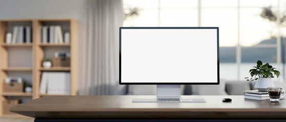 A white-screen computer mockup on a wooden desk in a contemporary living room. - obrazy, fototapety, plakaty