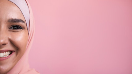 Joyful smile. Happy emotion. Half face portrait of amused satisfied pleased cheerful woman in hijab isolated on pink empty space background.