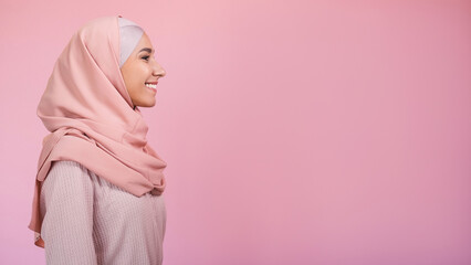 Happy woman. Modest beauty. Positive emotion. Side view portrait of pleased smiling girl in hijab isolated on pastel pink empty space background.