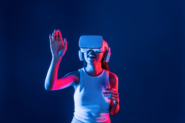 Smart female standing in cyberpunk neon light wear VR headset connecting metaverse, futuristic cyberspace community technology. Elegant woman use hand touching generated virtual object. Hallucination.