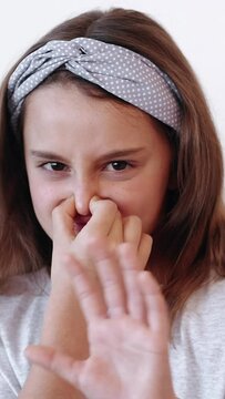Vertical video. Disgusted child. Yuck kid. Dissatisfied picky naughty little girl pinching nose to avoid bad smell showing stop sign isolated on white background.