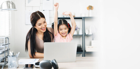 Excited small daughter celebrating successful with mother  while  using laptop at table in light living room