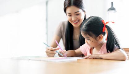 Happy  young mother smile with daughter in living room at home, teaching small daughter to reading and writing to develop her daughter skill. Home School Concept