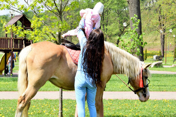 A young woman takes a little girl off a horse