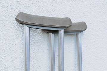 Grey metal crutches in foreground with white rough background. Concept of health and care. Walking...