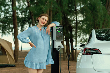 Holiday road trip vacation traveling to the beach camp with electric car, young woman recharge EV...
