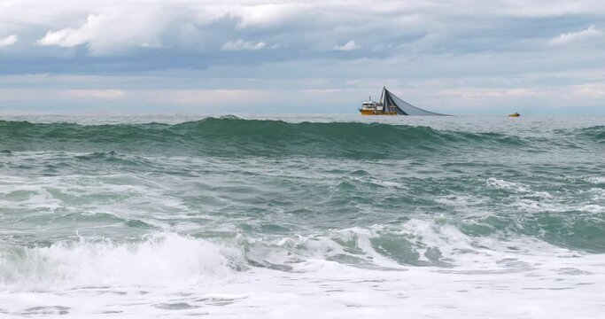 Footage of fishing boat fishing in wavy sea.