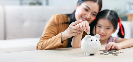 Happy family mom and little daughter saves money in a piggy bank pig.