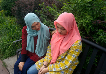 Asian muslim woman encouraging her friend who have a critical problem while sitting on bench at the...