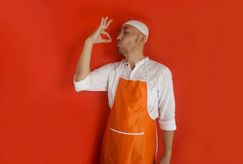 Asian man wear skullcap and apron, making delicious gesture with finger, side view