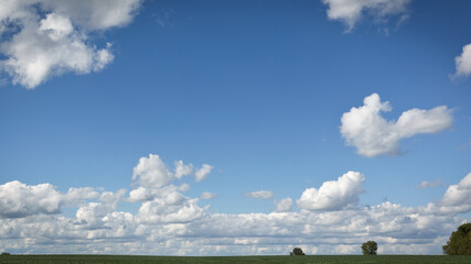 Horizontal color photo of white cumulus clouds over an agricultural field on a warm sunny day.