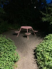 Pink round table with five seats in a park late at night.